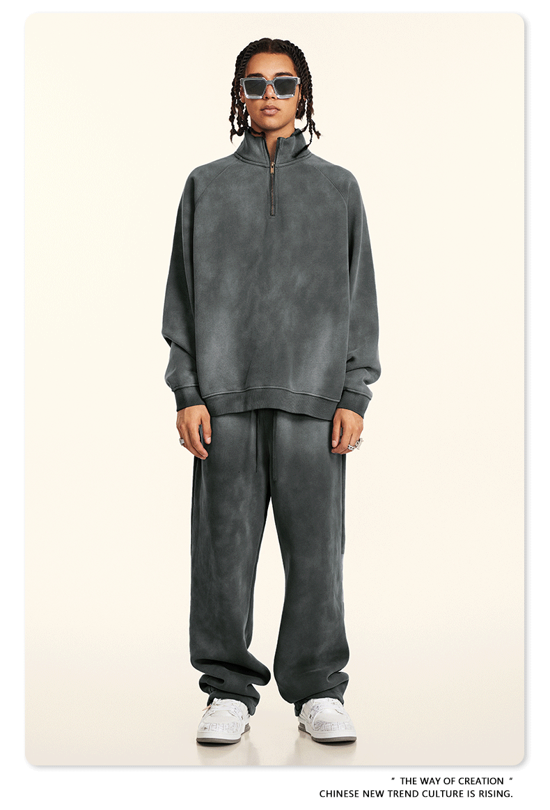 Model with twisted hair in slate gray half-zip pullover and matching pants, square sunglasses, silver jewelry, white sneakers