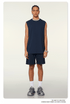 Model wearing navy blue matching set with sleeveless top and shorts, silver chain necklace, white socks and sneakers on neutral background