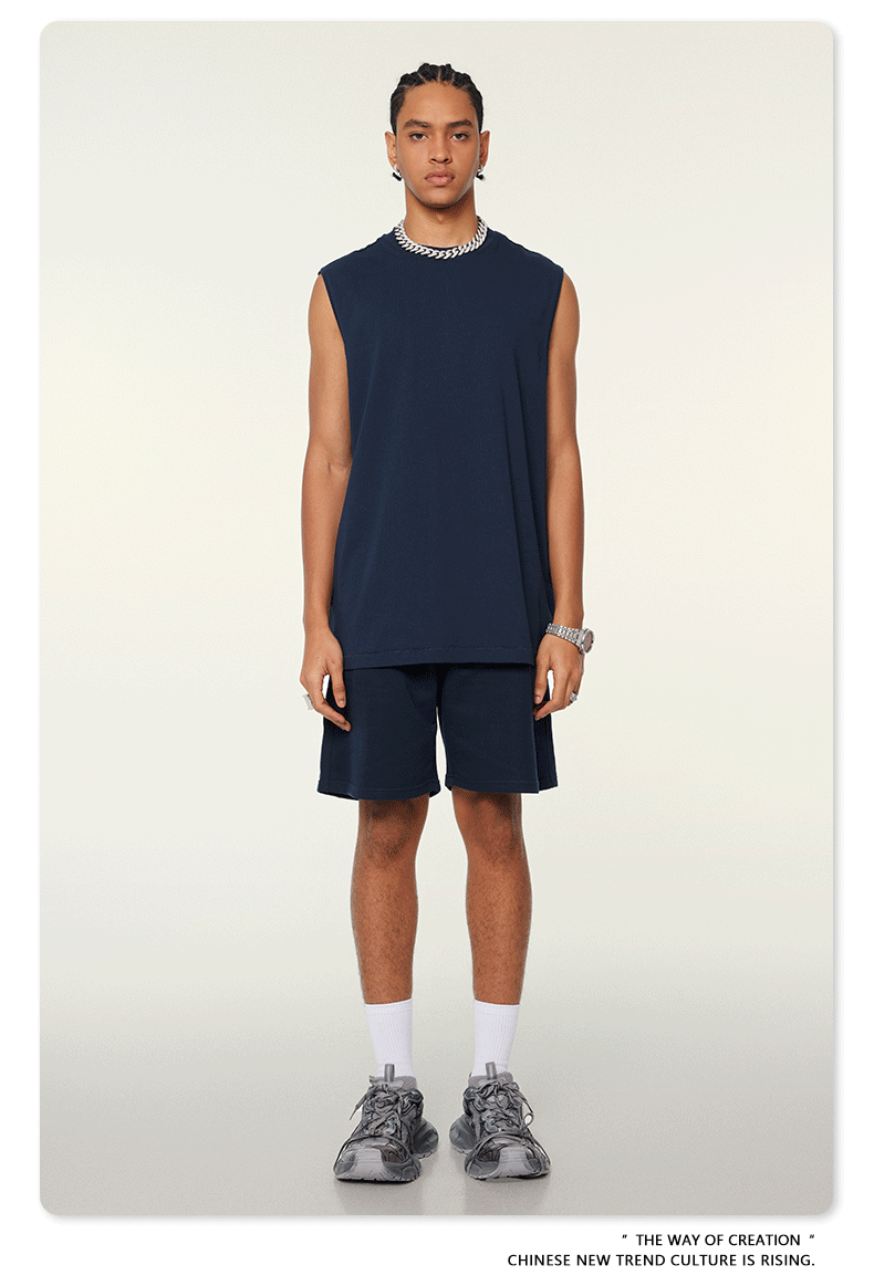 Model wearing navy blue matching set with sleeveless top and shorts, silver chain necklace, white socks and sneakers on neutral background