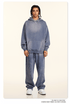 Model with twisted braids wearing blue-gray sweatsuit set with oversized hoodie and matching pants against cream background