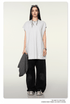 Model with dark hair wearing oversized white t-shirt and black wide-leg pants with silver sneakers against cream background
