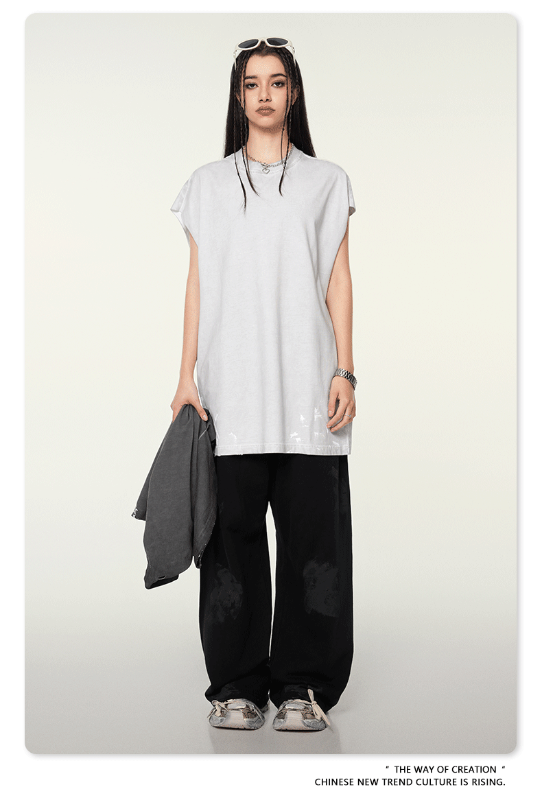 Model with dark hair wearing oversized white t-shirt and black wide-leg pants with silver sneakers against cream background