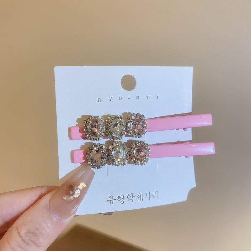 Pink alligator clips with two large heart-shaped crystals, accented with rhinestones, displayed on a card.