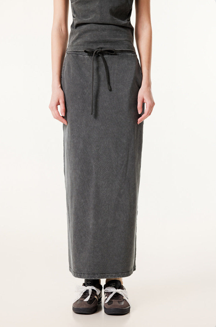 Long dark gray denim skirt with drawstring waist and side pockets, paired with gray and black sneakers with white laces