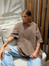 Person wearing a brown oversized shirt and light blue jeans sitting on a couch.