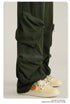 Close-up of olive green cargo pants pocket detail with zippered utility pouch and cream sneakers with orange detail