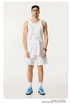 Model in all-white outfit with a tank top, shorts, and blue sneakers, accessorized with sunglasses and a watch