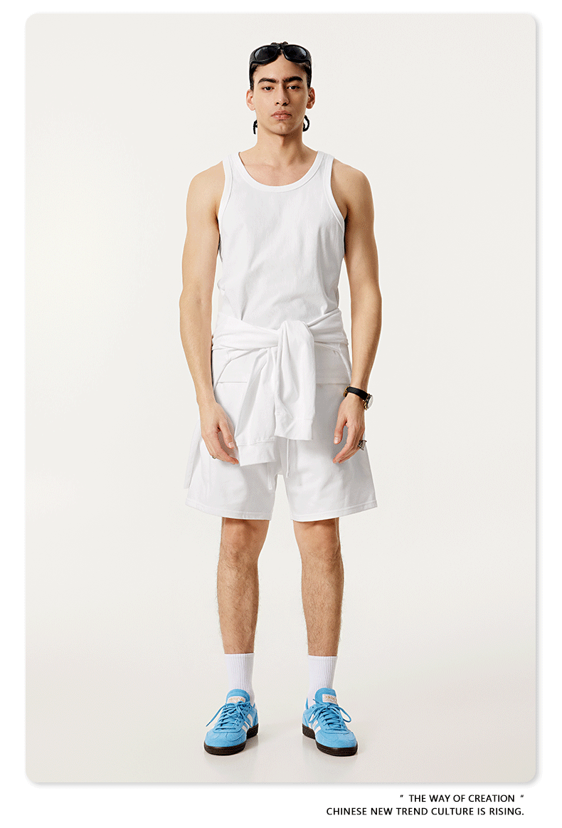 Model in all-white outfit with a tank top, shorts, and blue sneakers, accessorized with sunglasses and a watch