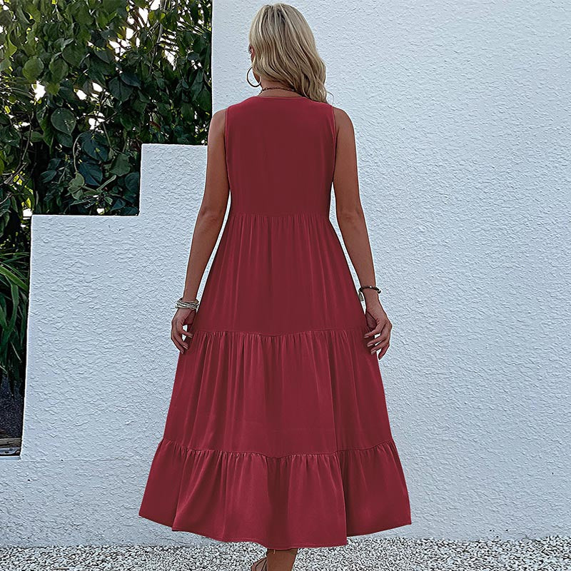 A woman is wearing a burgundy maxi dress with tiered skirt design, shown from back view against a white stucco wall