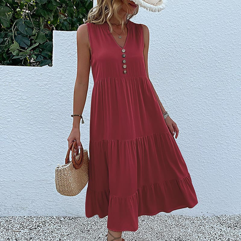A woman is wearing a navy tiered maxi dress with v-neckline, posing with one hand on her hip against a textured white wall