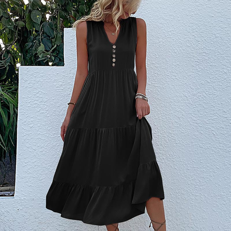 A woman is wearing a charcoal tiered midi dress with button detail, standing with hand on hip against a white textured wall