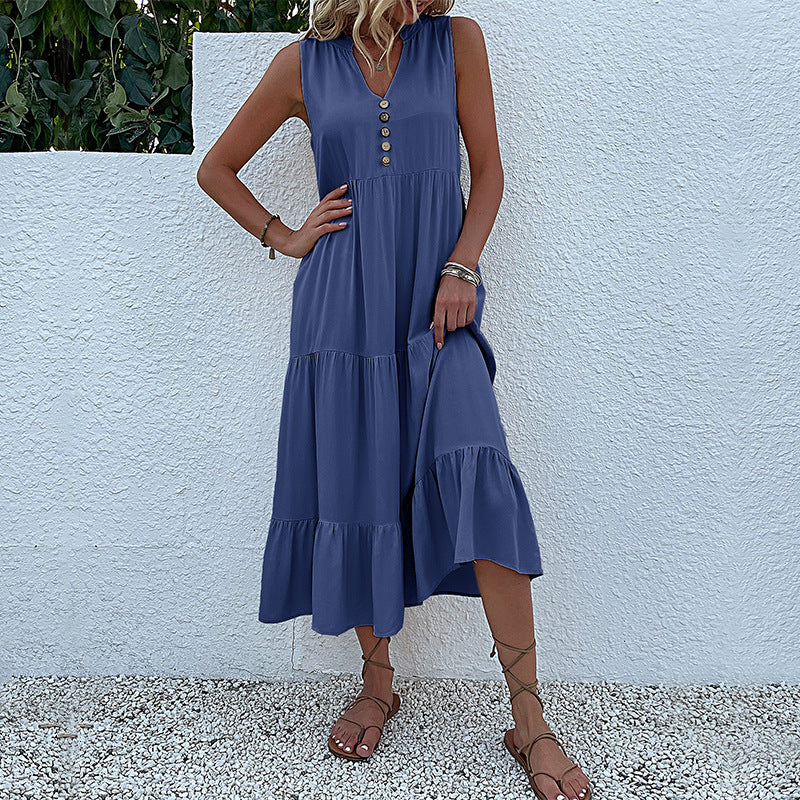 A woman is wearing a navy tiered dress with v-neck and button details, with hand on hip against a white stucco background