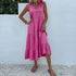 A woman is wearing a hot pink tiered midi dress with v-neck, posing with hand on hip against a textured white wall