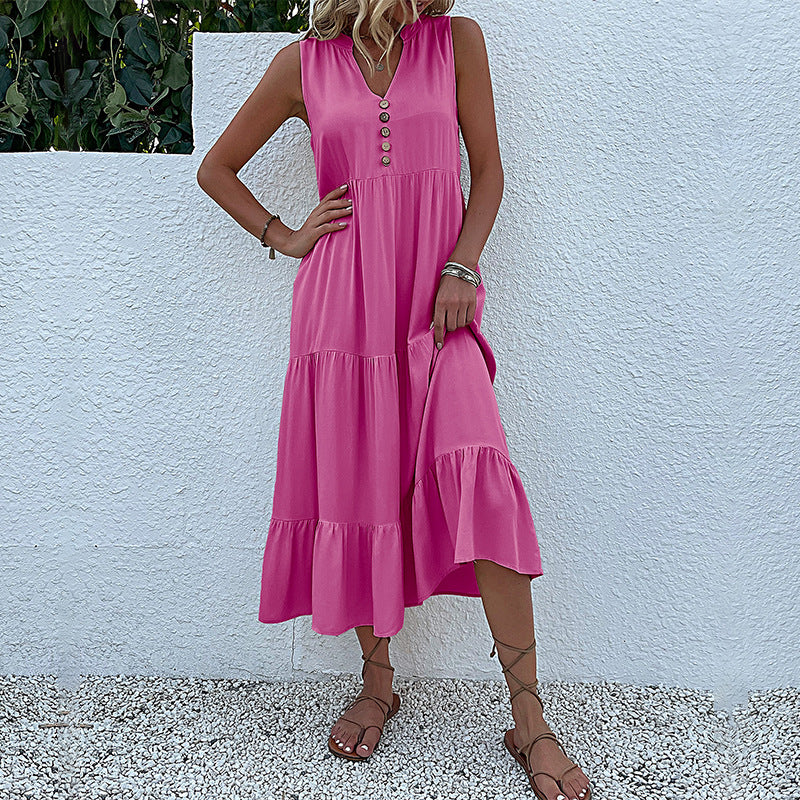 A woman is wearing a hot pink tiered midi dress with v-neck, posing with hand on hip against a textured white wall