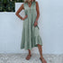 A woman is wearing a sage green v-neck tiered dress, posing with hand on hip against a white stucco wall background