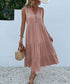 A woman is wearing a blush tiered midi dress with decorative front buttons, holding a straw basket against a white wall
