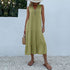 A woman is wearing a sage green tiered maxi dress with v-neck and button detail, carrying a straw bag against a white wall