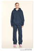 Model wearing pure white oversized zip-up hoodie and matching relaxed-fit sweatpants with silver chain necklaces and white sneakers against cream background