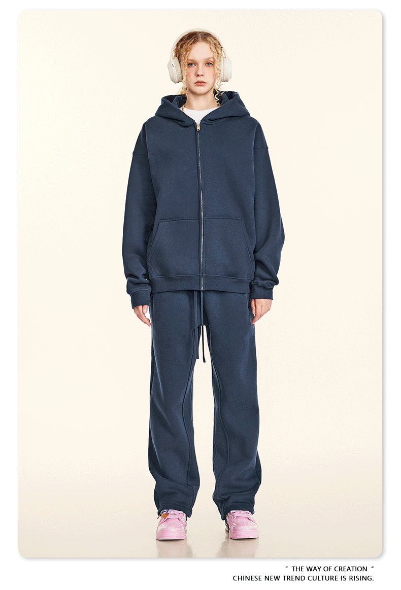 Model wearing pure white oversized zip-up hoodie and matching relaxed-fit sweatpants with silver chain necklaces and white sneakers against cream background