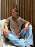 Person wearing a brown oversized sweater and blue jeans sitting on a couch.