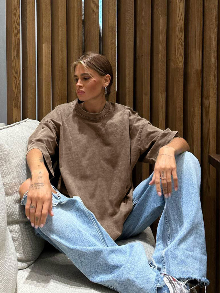 Person wearing a brown oversized sweater and blue jeans sitting on a couch.