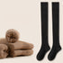 Black knee-high socks displayed with folded brown socks and red indicator button on beige background