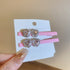 Pink alligator hair clips with a single heart-shaped crystal and rhinestone trim, displayed on a card.