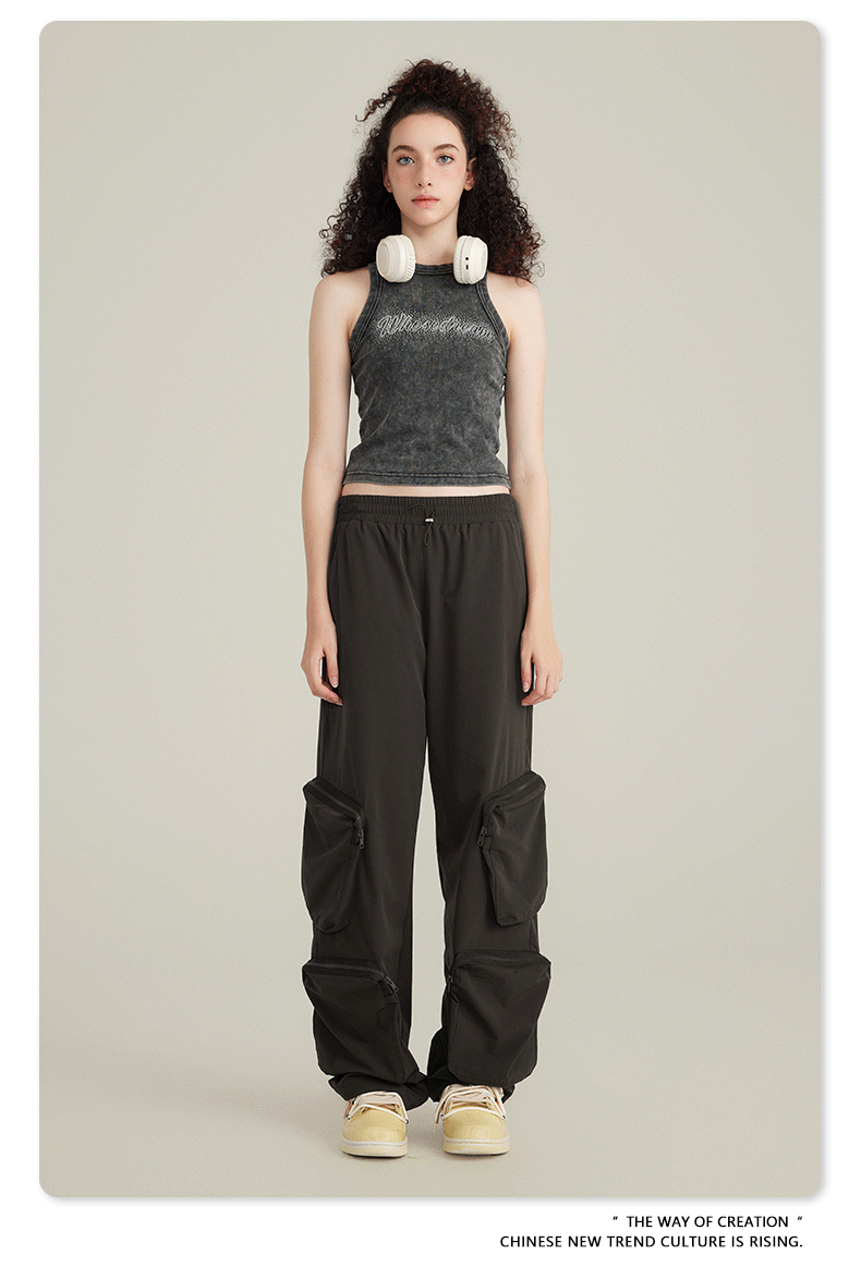 Model with curly dark hair wearing vintage-wash tank top with text graphic and black cargo pants with utility pockets on neutral background