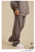 Side profile showing grey zip-up jacket sleeve and drawstring sweatpants with white sneakers on beige background with roses