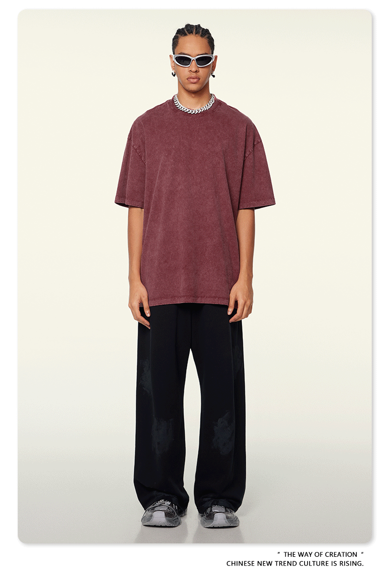 Model wearing burgundy oversized t-shirt with black wide-leg pants, white sunglasses and silver chain necklace against beige background