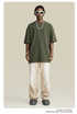 Model in olive t-shirt, white wide-leg pants, white sunglasses, silver chain against beige background
