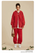 Woman with curly updo wearing red zip-up hoodie and matching sweatpants with small shoulder bag.gif