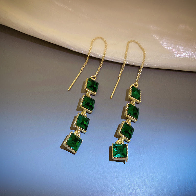 Long gold chain earrings with emerald green square-cut gemstones, suspended in a delicate linear design