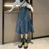 A woman is wearing a high-waisted blue denim midi skirt with diagonal seams, a white cropped sweater, and olive-green platform boots