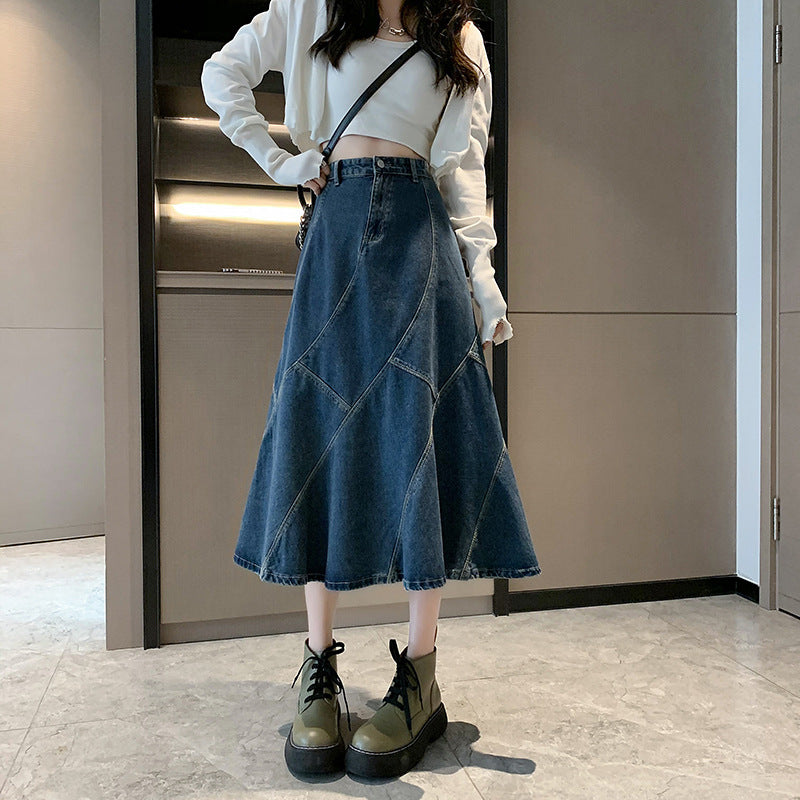 A woman is wearing a dark blue denim A-line midi skirt with visible stitching, a white cropped top, and olive-green platform boots