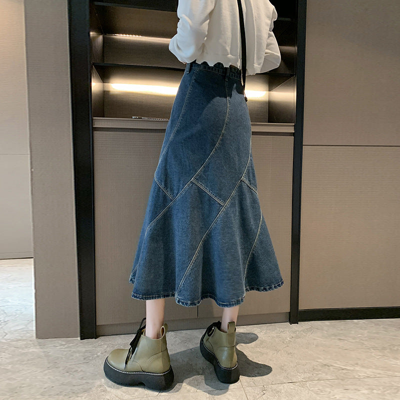 A woman is wearing a blue denim midi skirt with paneled stitching, a white cropped top, and chunky olive-green lace-up boots