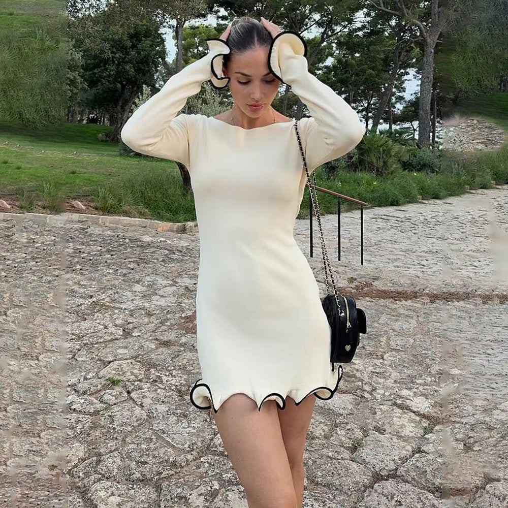 Woman wearing cream long-sleeve mini dress with black contrast ruffle trim, styled with small black handbag