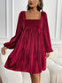 A woman in a burgundy velvet empire waist dress with puffy sleeves stands by a white sofa, showing the textured ribbed fabric