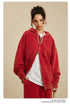 Close-up of woman in red zip-up hoodie with white t-shirt and beaded necklace against beige background