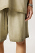 A close-up of light sage green cotton shorts with drawstring waist showing fabric detail and stitching against neutral background
