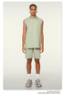 Model wearing mint green matching set with sleeveless top and shorts, white headphones, silver chain necklace and chunky sneakers on neutral background