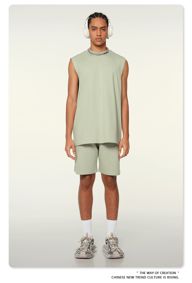 Model wearing mint green matching set with sleeveless top and shorts, white headphones, silver chain necklace and chunky sneakers on neutral background