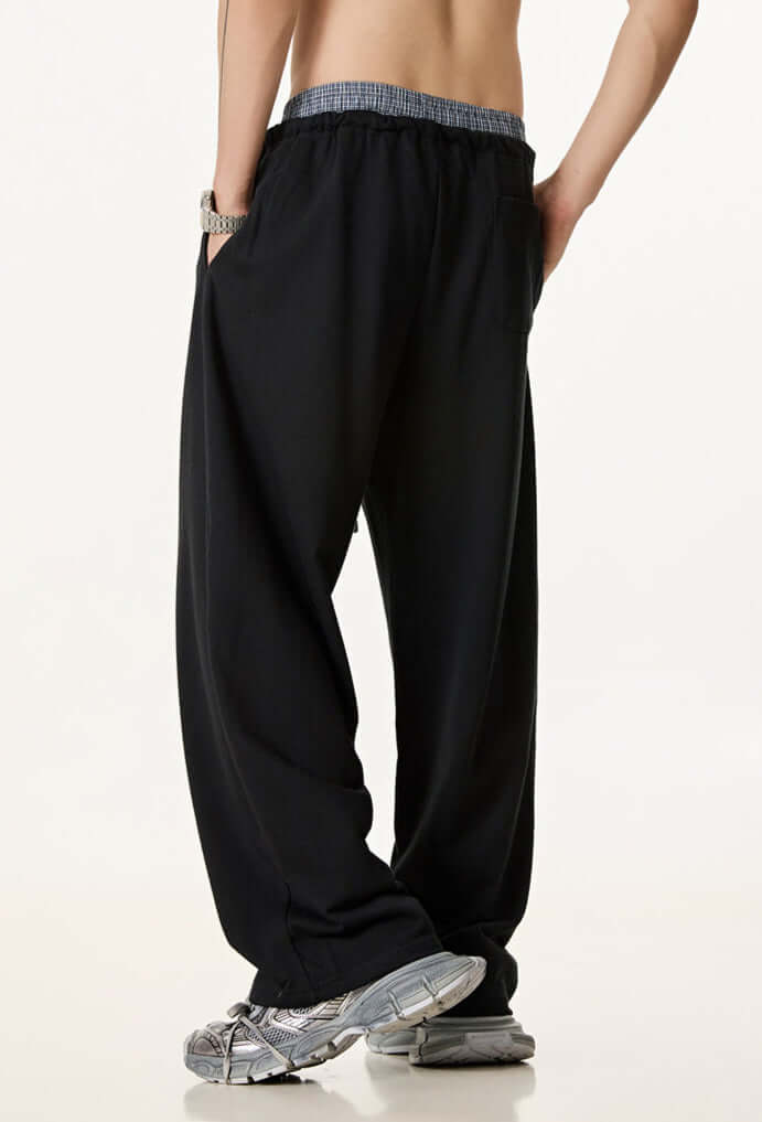 Rear view of black wide-leg sweatpants with an elastic waistband and single back pocket, styled with grey sneakers.