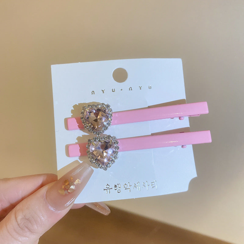 Pink alligator clips with double small heart-shaped crystals, accented with rhinestones, displayed on a card.