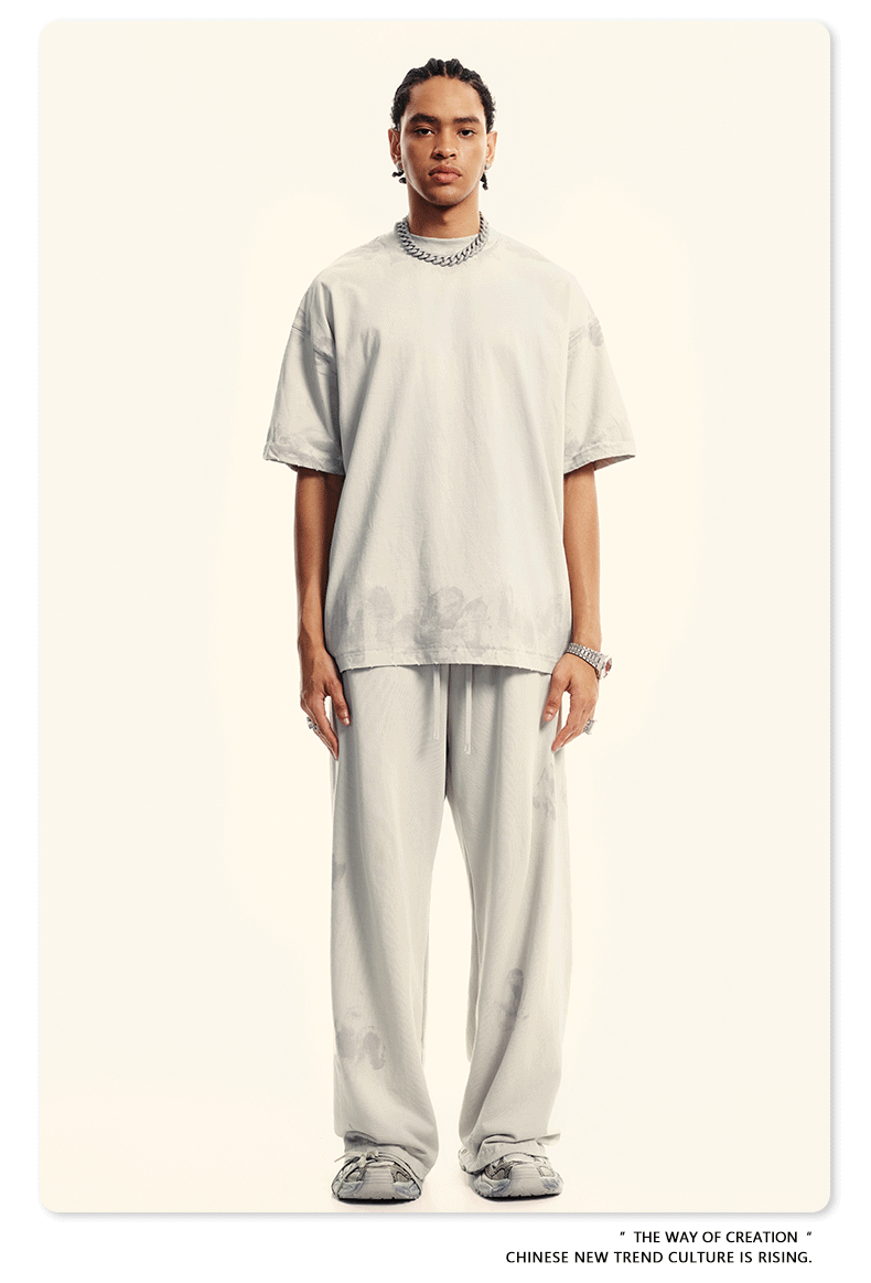 Model in cream two-piece set featuring oversized t-shirt and wide-leg pants with subtle wash effect. Styled with silver chain necklace and statement watch