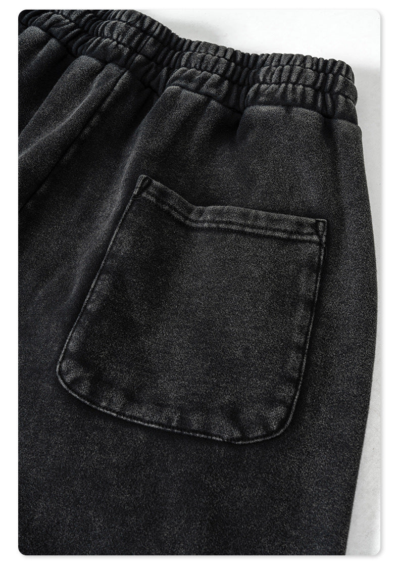 Close-up of elastic waistband and back pocket detail on black track pants against white studio background