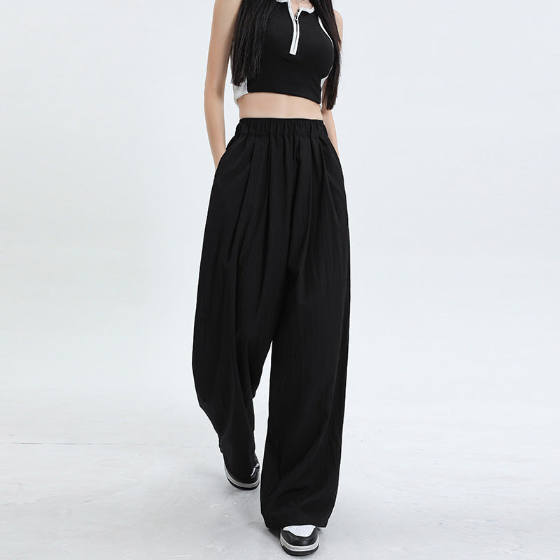 Black wide-leg pants with elastic waist and roomy silhouette, shown with black zip-front crop top and platform sneakers