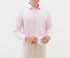 A model is holding a white coffee mug while wearing a light pink dress shirt and cream trousers. Gold watch visible on wrist