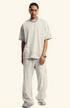 Front view of model in light beige oversized t-shirt and matching pants. Silver accessories include chain necklace and red-faced watch