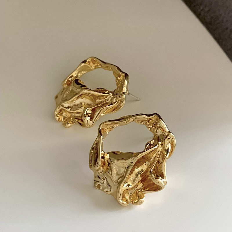 Sculptural Gold Hoop Earrings – Artistic gold earrings with an irregular molten-metal design, set against a neutral background